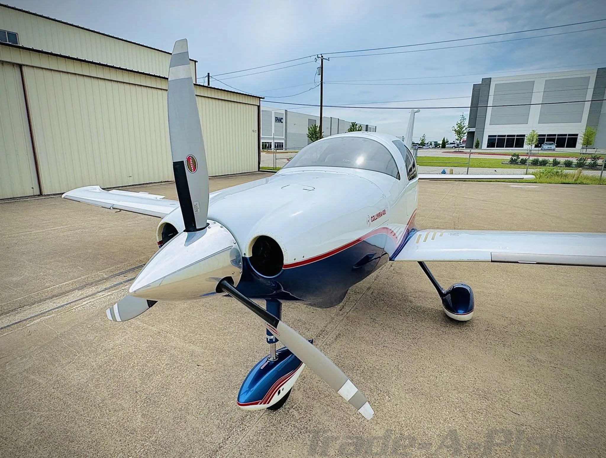 Front-left view of a white and blue Columbia 400 with red stripes on an airport apron.