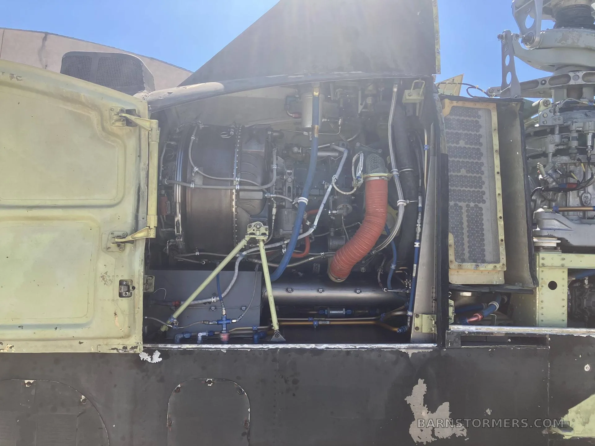 A detailed view of a helicopter's engine compartment, showing the turbine engine and various pipes and connections.