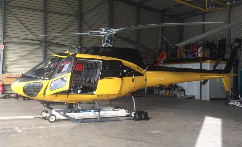 A yellow helicopter with black accents and open doors sits in a hangar.