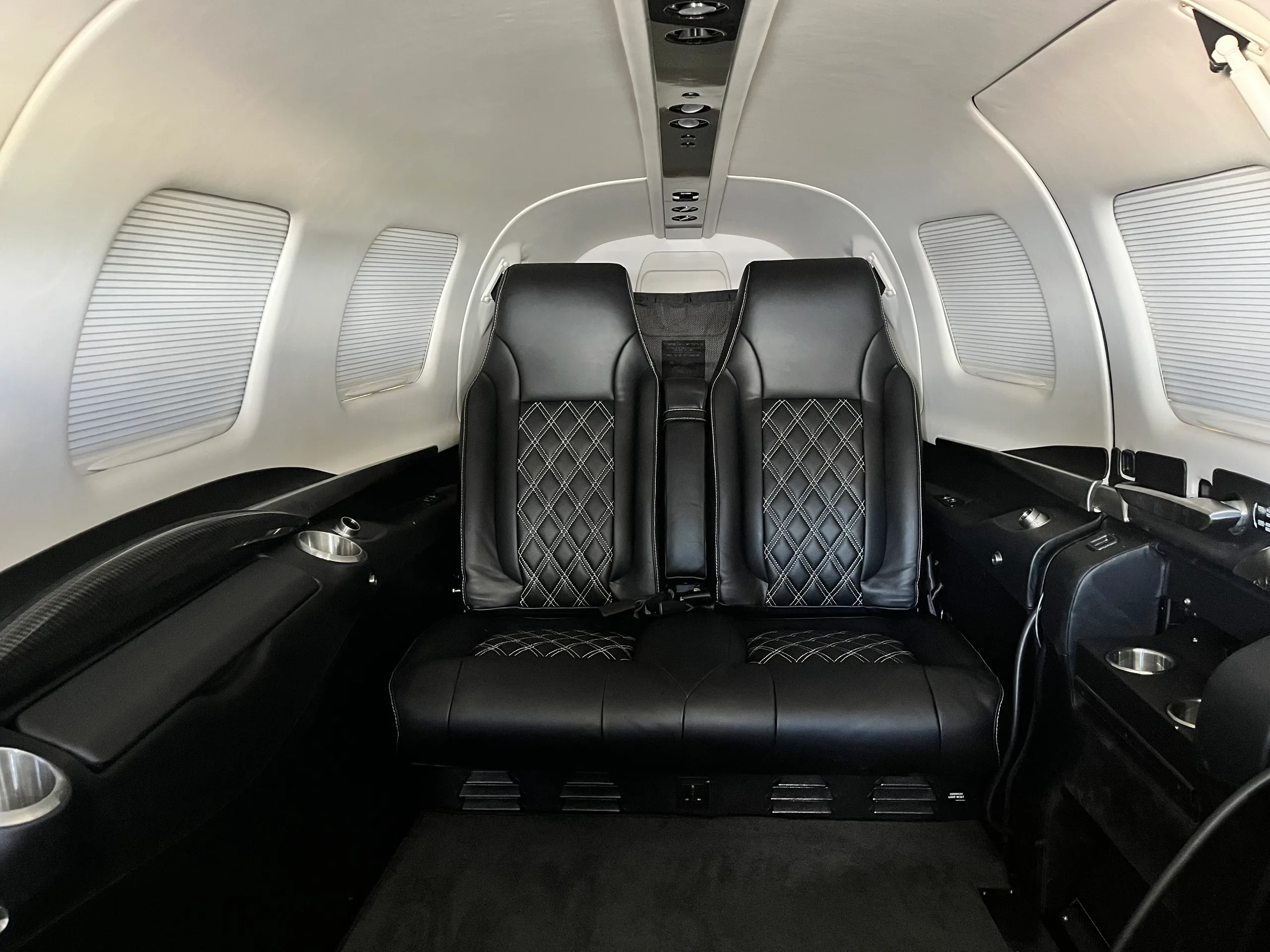 The black leather interior cabin seats with white diamond stitching inside a small aircraft.