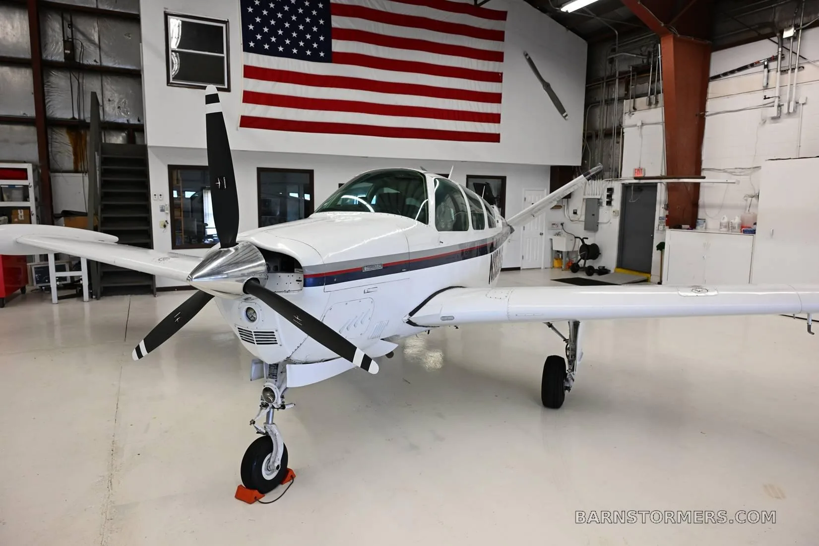 Front view of a white single-engine aircraft with a propeller, registration N322HS, parked in a hangar.