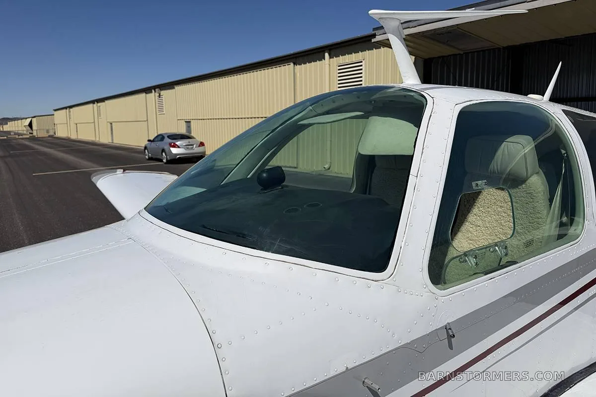 A close-up view of the cockpit windshield and side window of a white Beechcraft Baron, showing the interior seats.