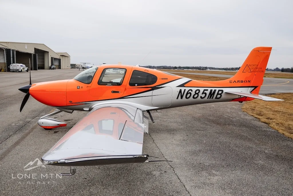 A three-quarter view of the orange and silver Cirrus SR20 aircraft N685MB on an airfield.