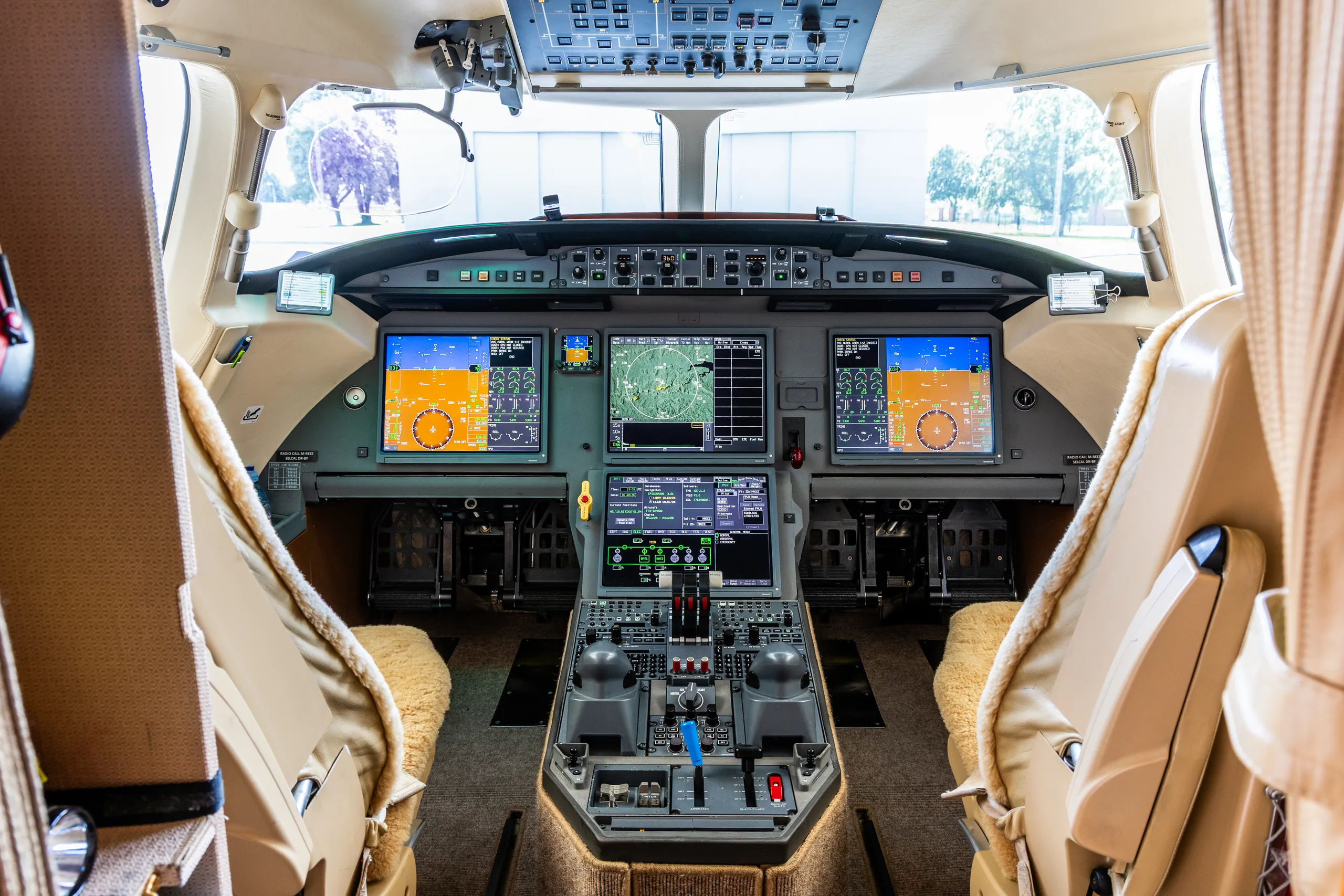 The modern cockpit of a business jet with multiple digital displays, control yokes, and a central throttle quadrant.