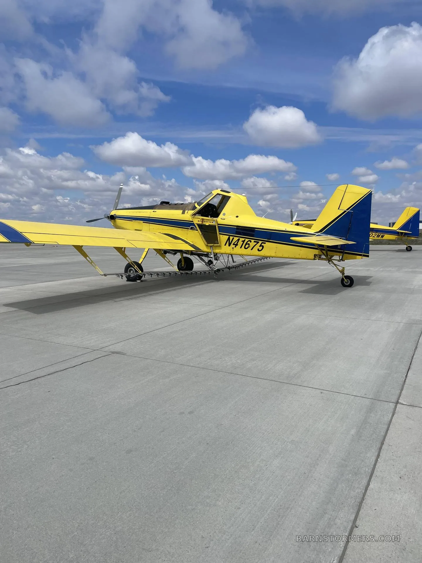 A yellow and blue Air Tractor agricultural aircraft with registration N41675 parked on a concrete tarmac under a partly cloudy sky.