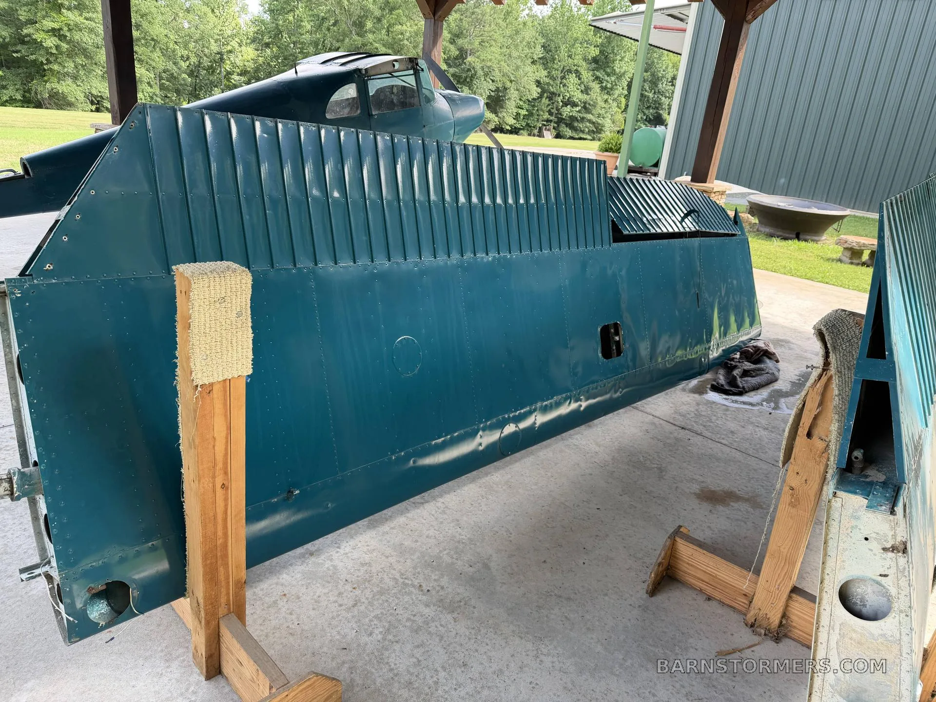 A large teal aircraft wing section on wooden stands, with the aircraft fuselage visible in the background.