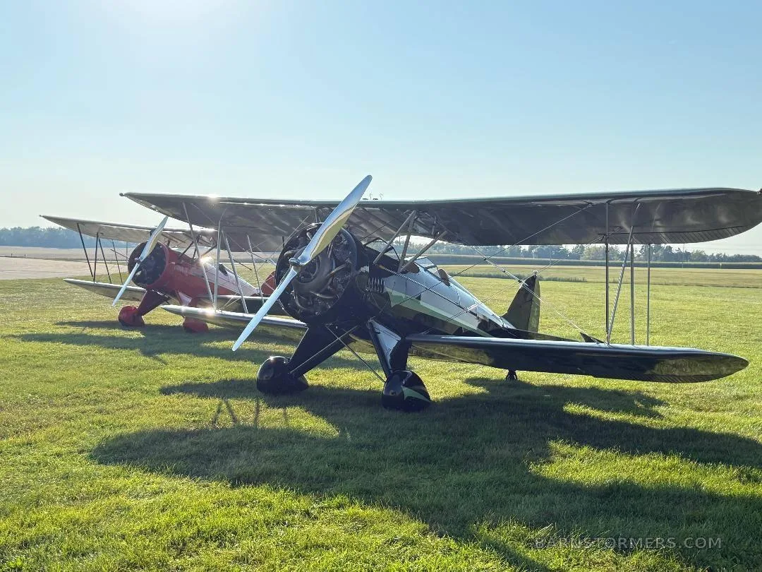 Two biplanes, one black and one red, are parked on a sunny green airfield.