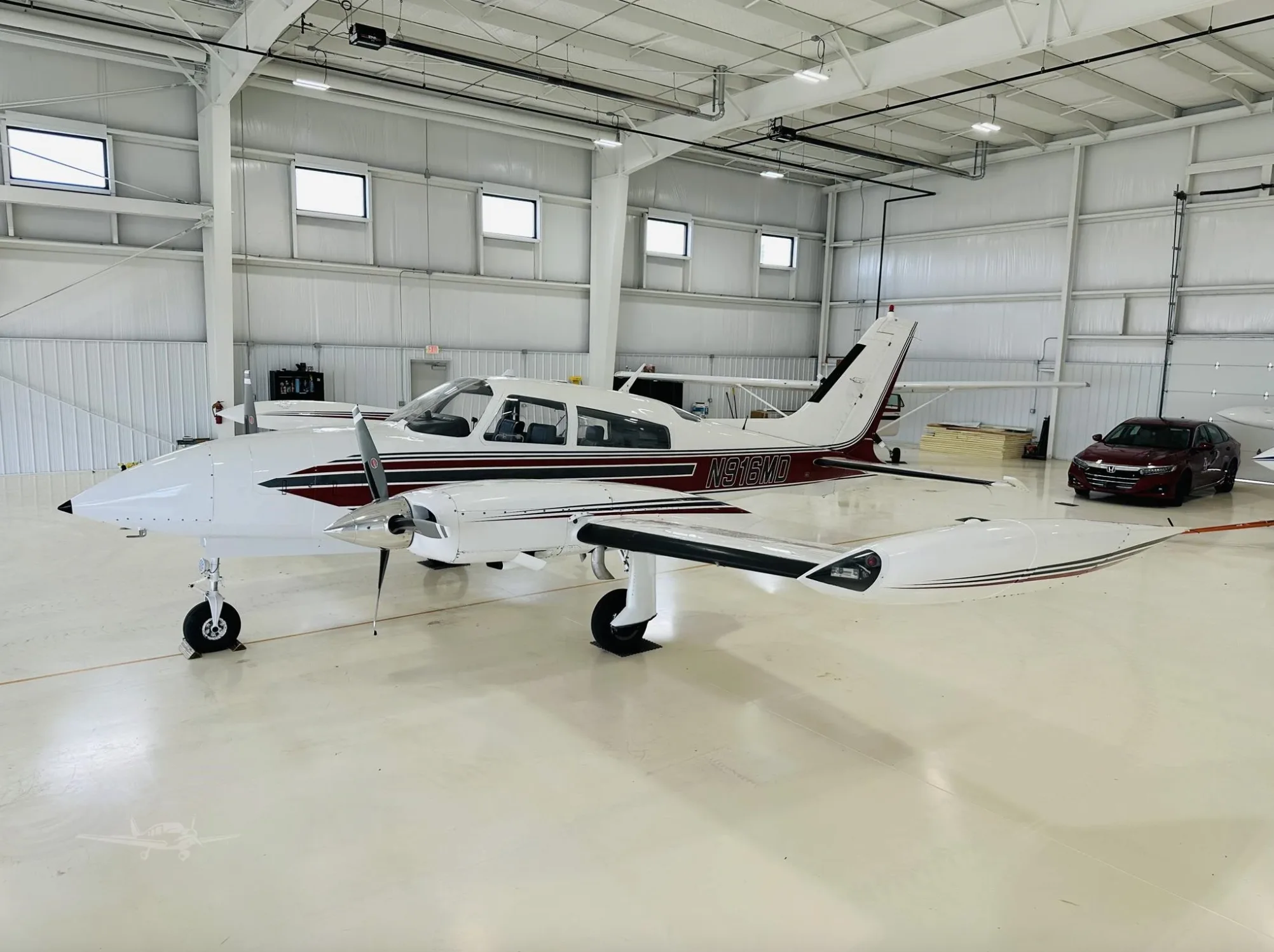 A white and maroon twin-engine aircraft, N916MD, is parked in a well-lit hangar.