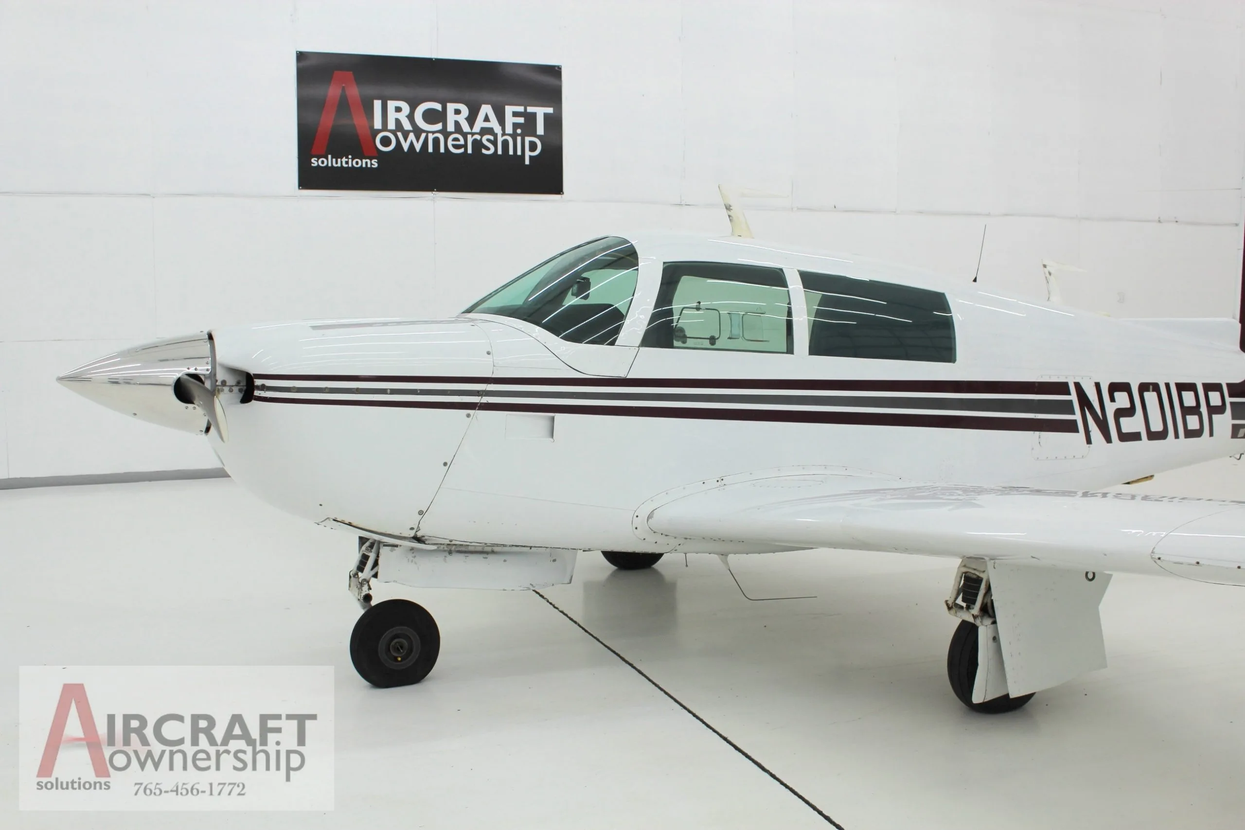 Close up of the front of the white and brown N201BP aircraft in a hangar.