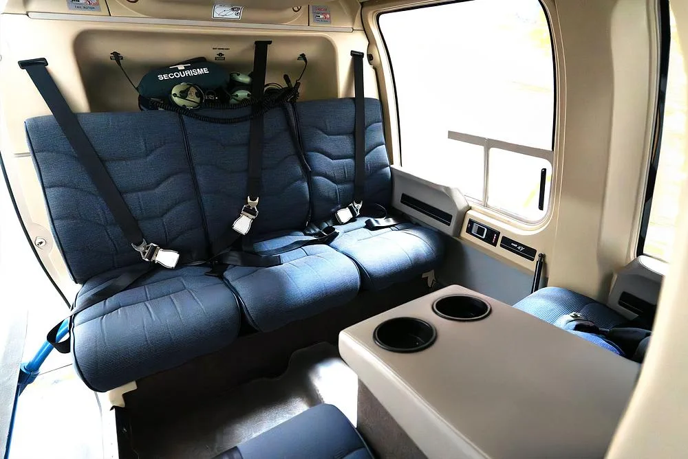 The rear cabin interior of the helicopter, featuring blue seats with seatbelts and a small table with cup holders.