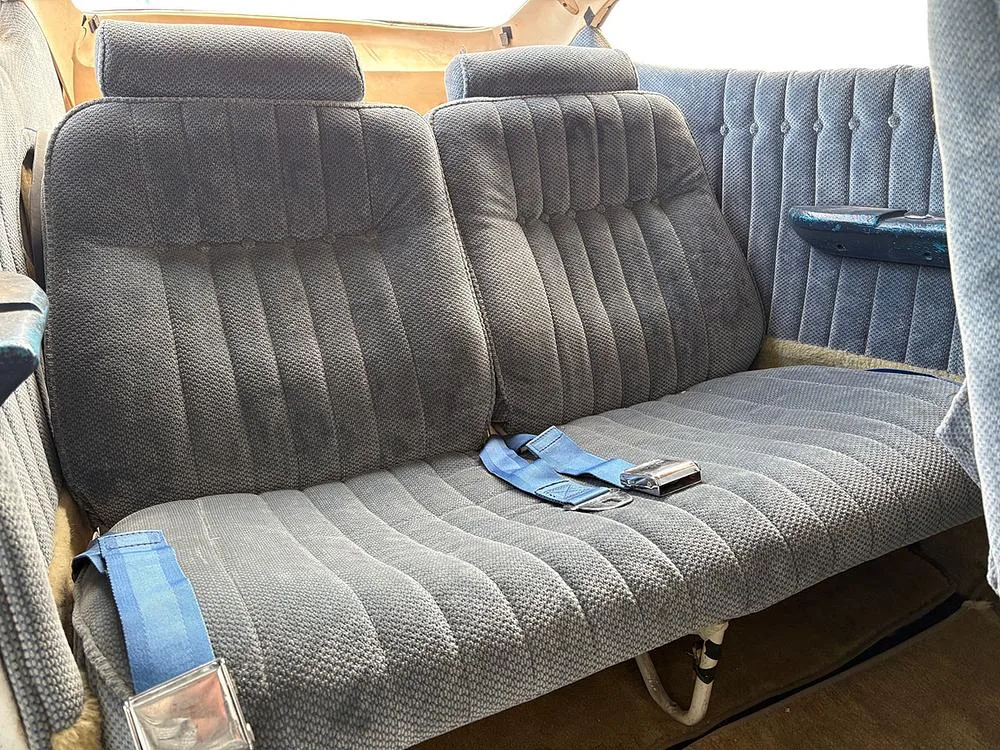 The rear blue fabric bench seat of an aircraft cabin with blue seatbelts.