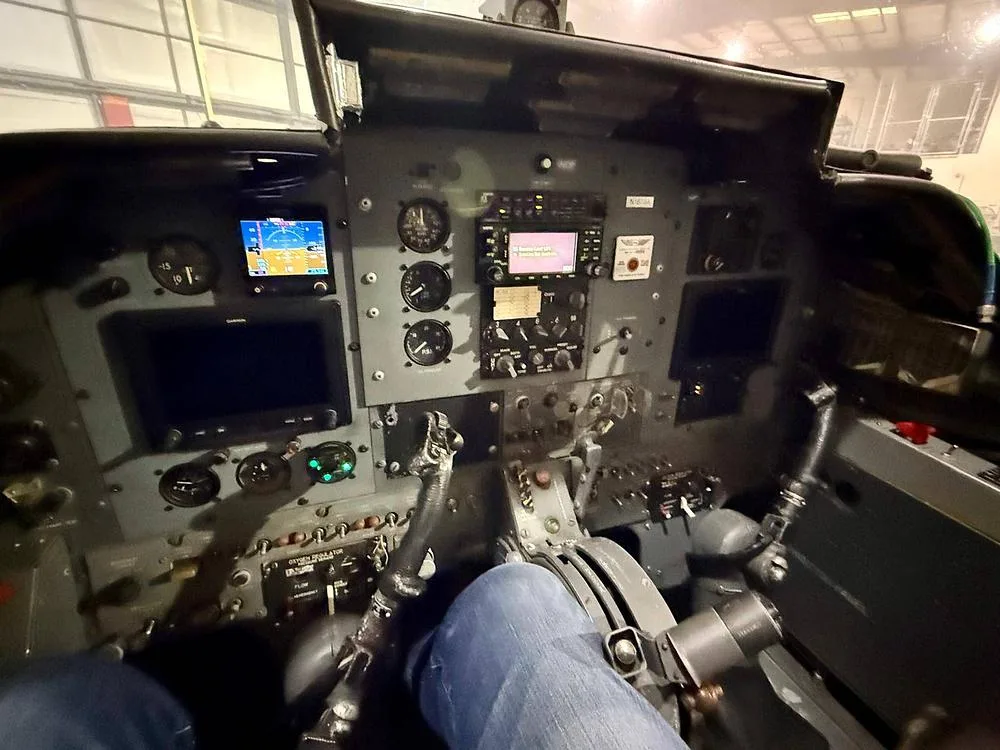 The cockpit of a BAC Strikemaster Mk.88 showing the instrument panel, controls, and a pilot's legs.
