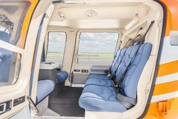 The interior cabin of an orange helicopter with blue quilted seats and large windows.
