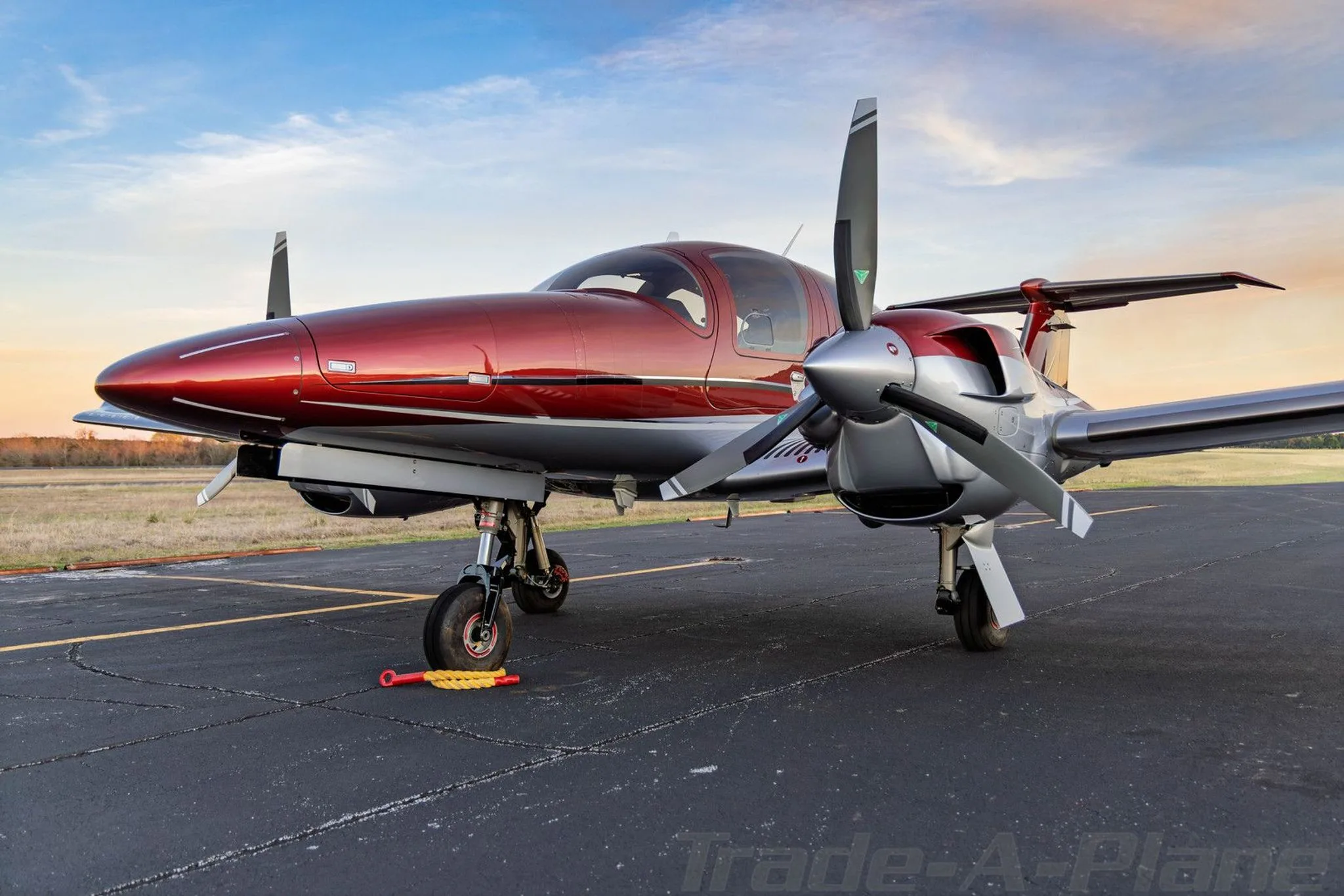 A front view of a red and silver Diamond DA62 aircraft showing its propellers and nose gear.