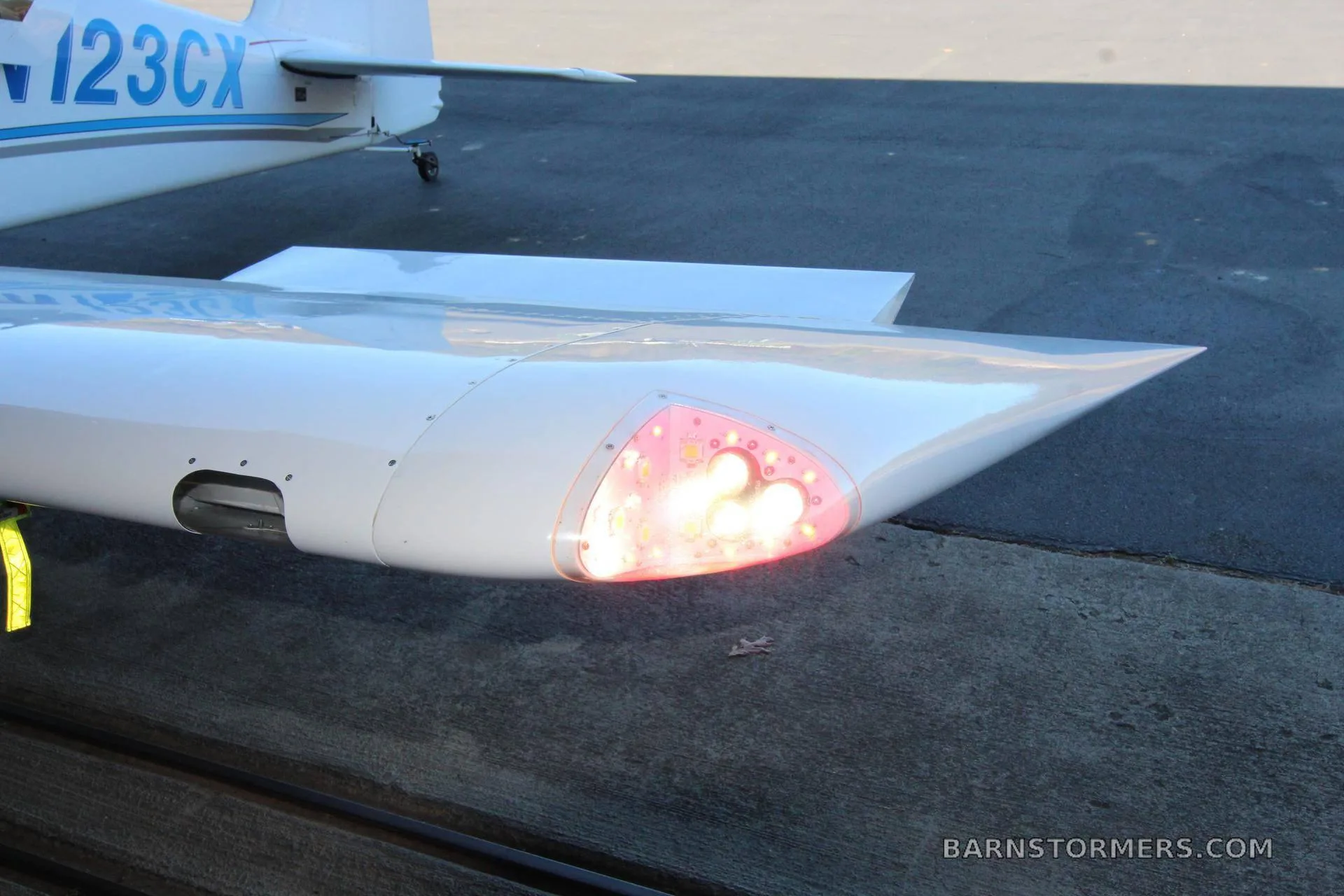 A close-up view of the white wingtip of an aircraft, showing a bright red navigation light.