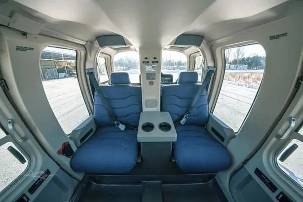 The helicopter's interior cabin features two rows of blue fabric seats with seatbelts and a center console with cup holders.