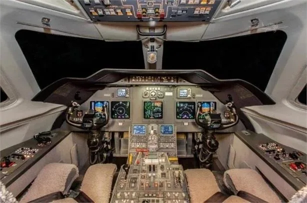The cockpit of a private jet, featuring a modern glass panel display with multiple screens and a complex array of controls.