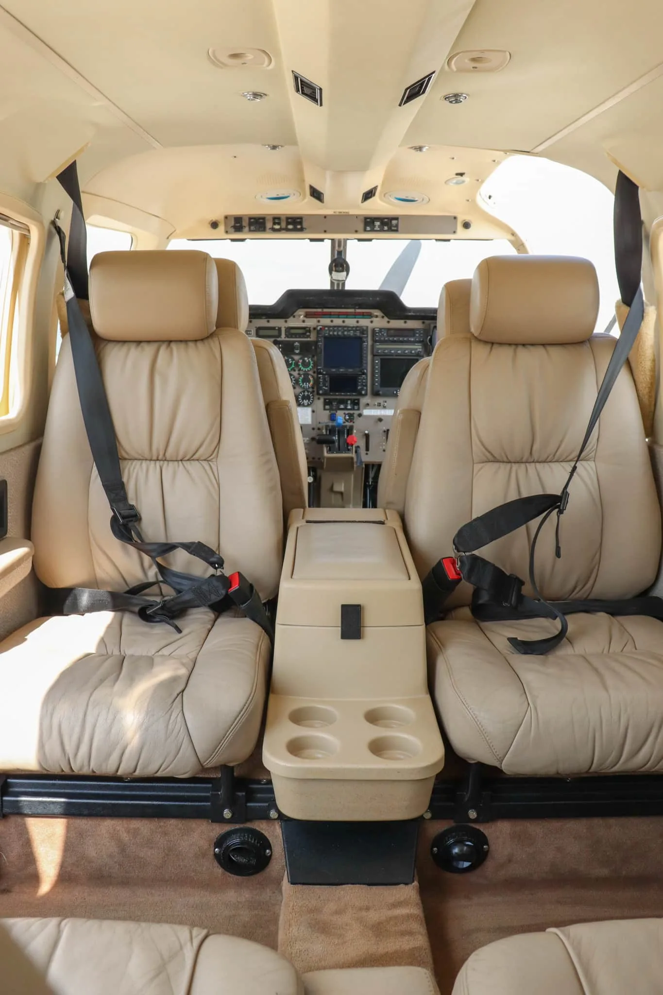 The aircraft cabin interior with light brown leather seats and a center console, looking towards the cockpit.