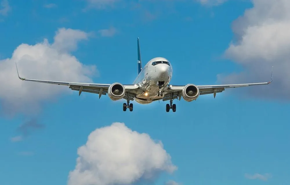 A silver Boeing 737 MAX aircraft with landing gear extended, approaching for landing against a blue sky with white clouds.