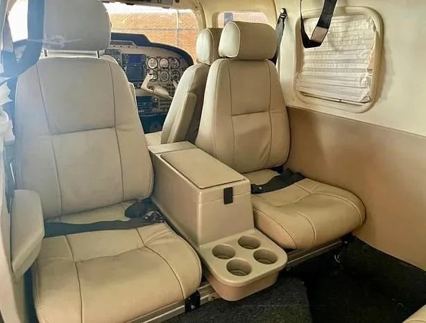 Two rows of light beige leather seats with a center console and cup holders are visible in the aircraft's cabin.