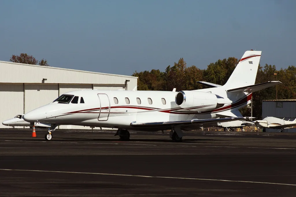A white jet aircraft parked on the tarmac with a red stripe.
