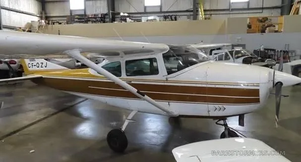 A white and gold Cessna 172 parked in a hangar, viewed from the front-right.