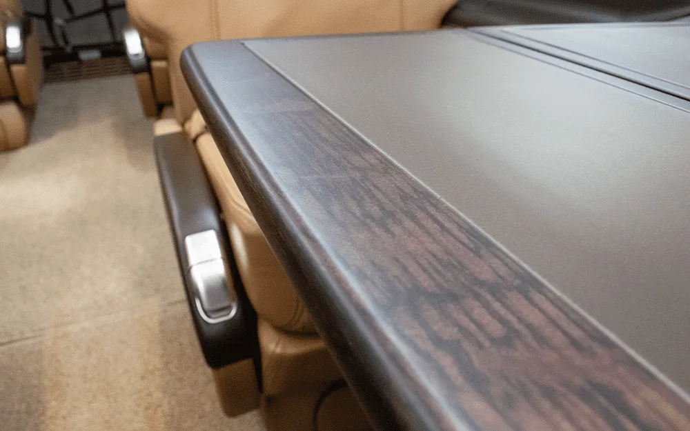 A close-up view of a dark wood-grain table surface and a tan leather seat armrest inside the aircraft cabin.