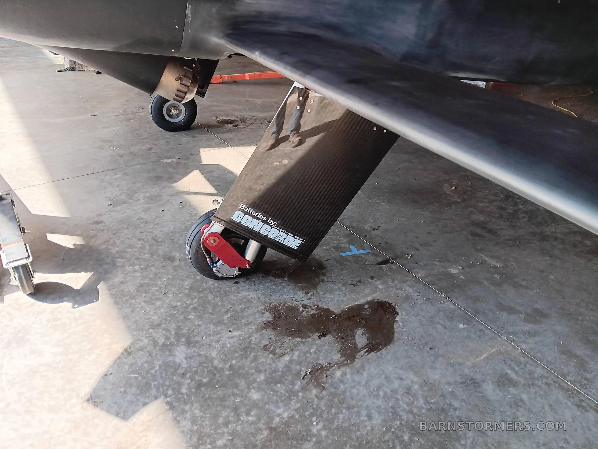 A close-up view of the main landing gear and wing of a dark aircraft, showing a 'Concorde Batteries' label on the gear fairing.