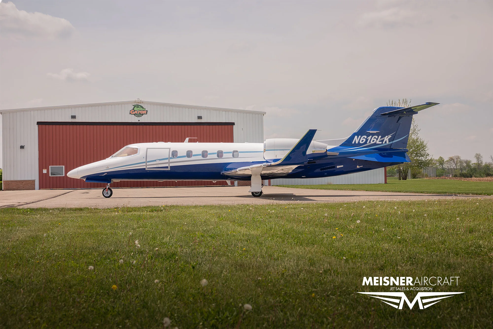 A white and blue Learjet N616LK parked in front of a hangar with a "Gator" logo.