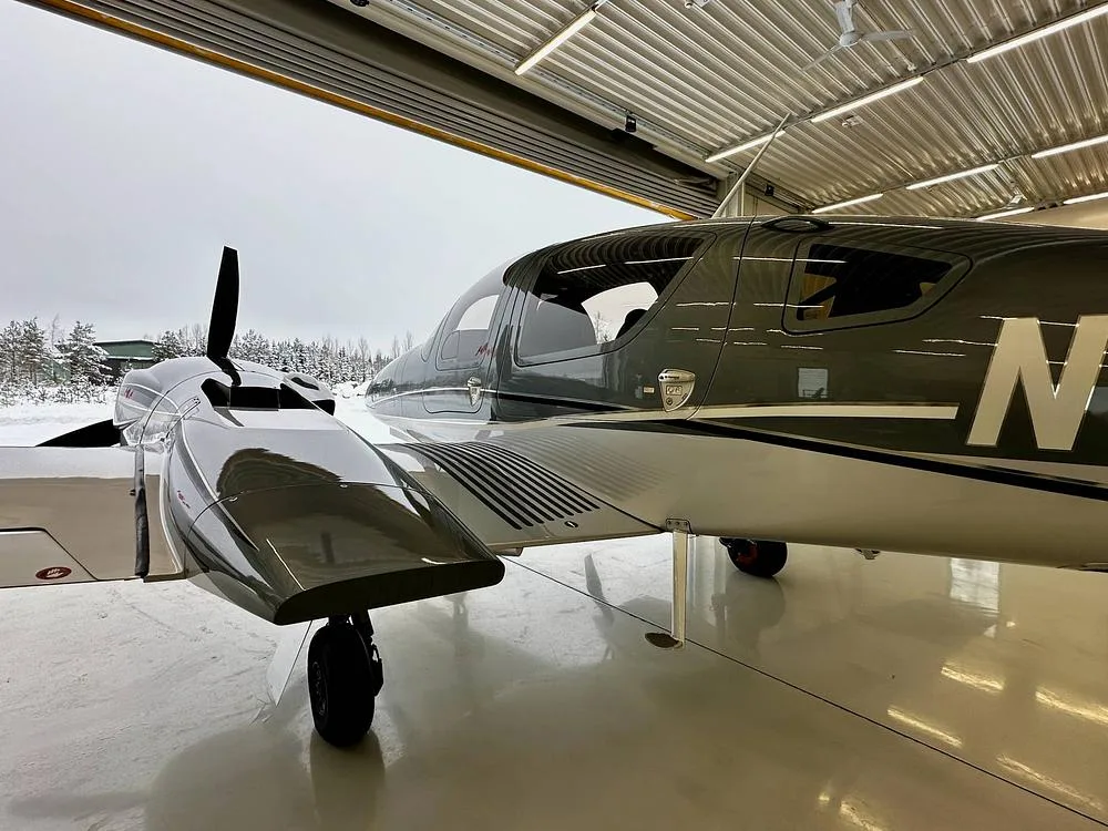 A close-up side view of the cockpit and engine nacelle of a gray and silver Diamond DA62 aircraft, partially in a hangar.
