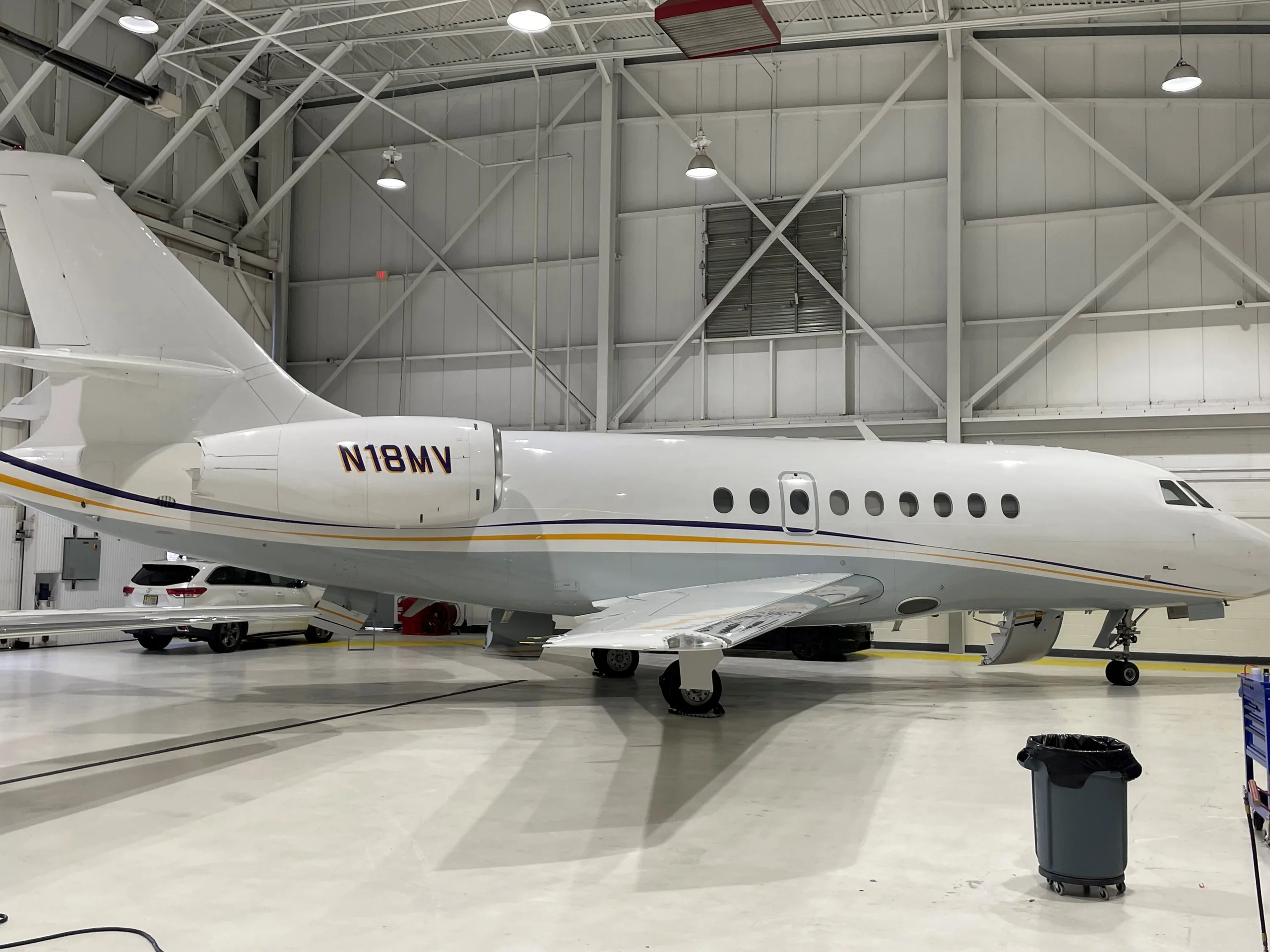 Side view of the aircraft N18MV in a hangar, showcasing its white and gray paint scheme with blue and gold stripes.