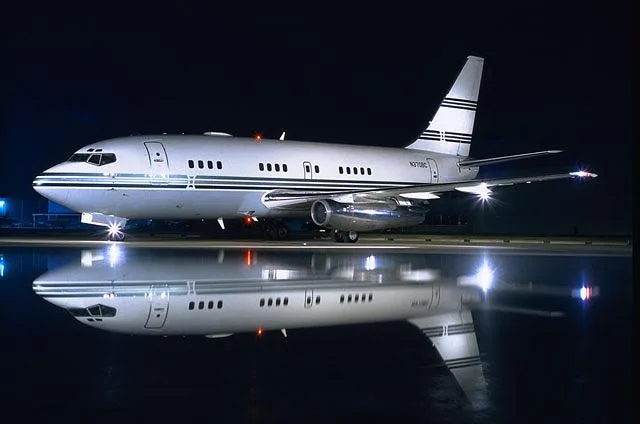 A silver Boeing 737 business jet (N370BC) is parked on a wet tarmac at night, reflecting in the surface.