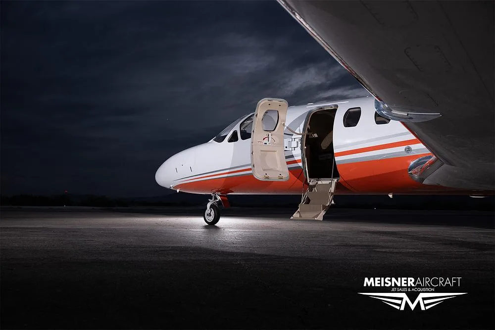 A close-up view of the front of a white and orange Cessna Citation Excel with its passenger door open, parked at night.