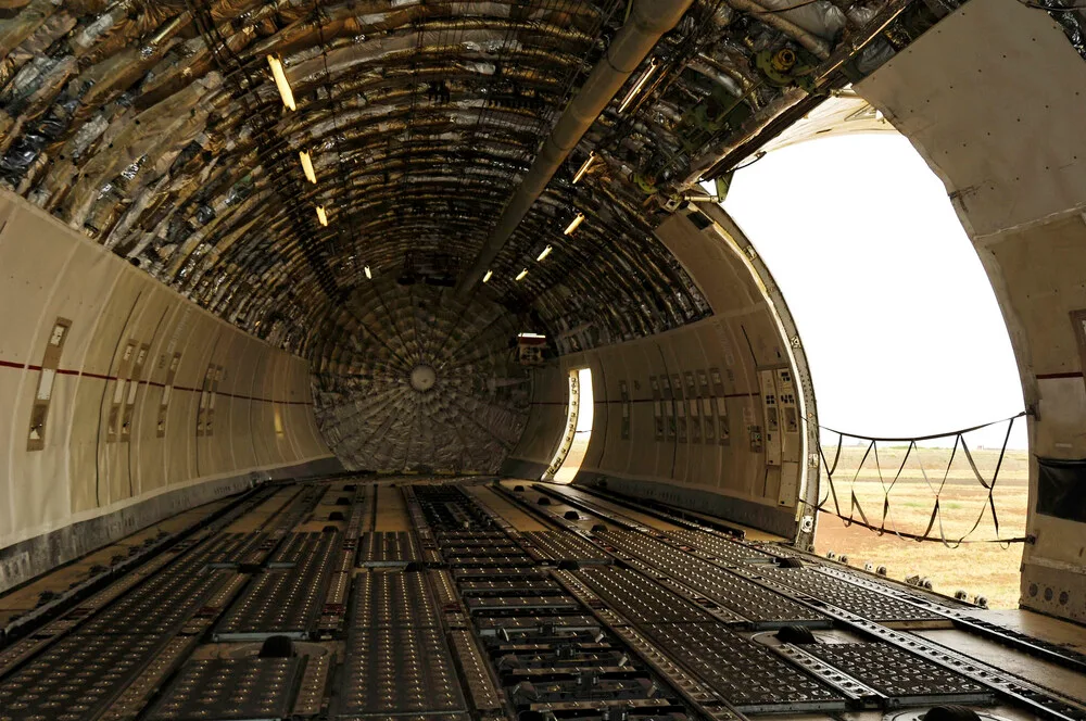 The vast, empty cargo hold of an aircraft, showing the floor tracks and an open side cargo door.