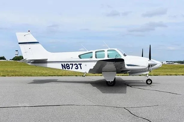 A white twin-engine Beechcraft Baron aircraft with blue stripes, registration N873T, parked on an asphalt runway.