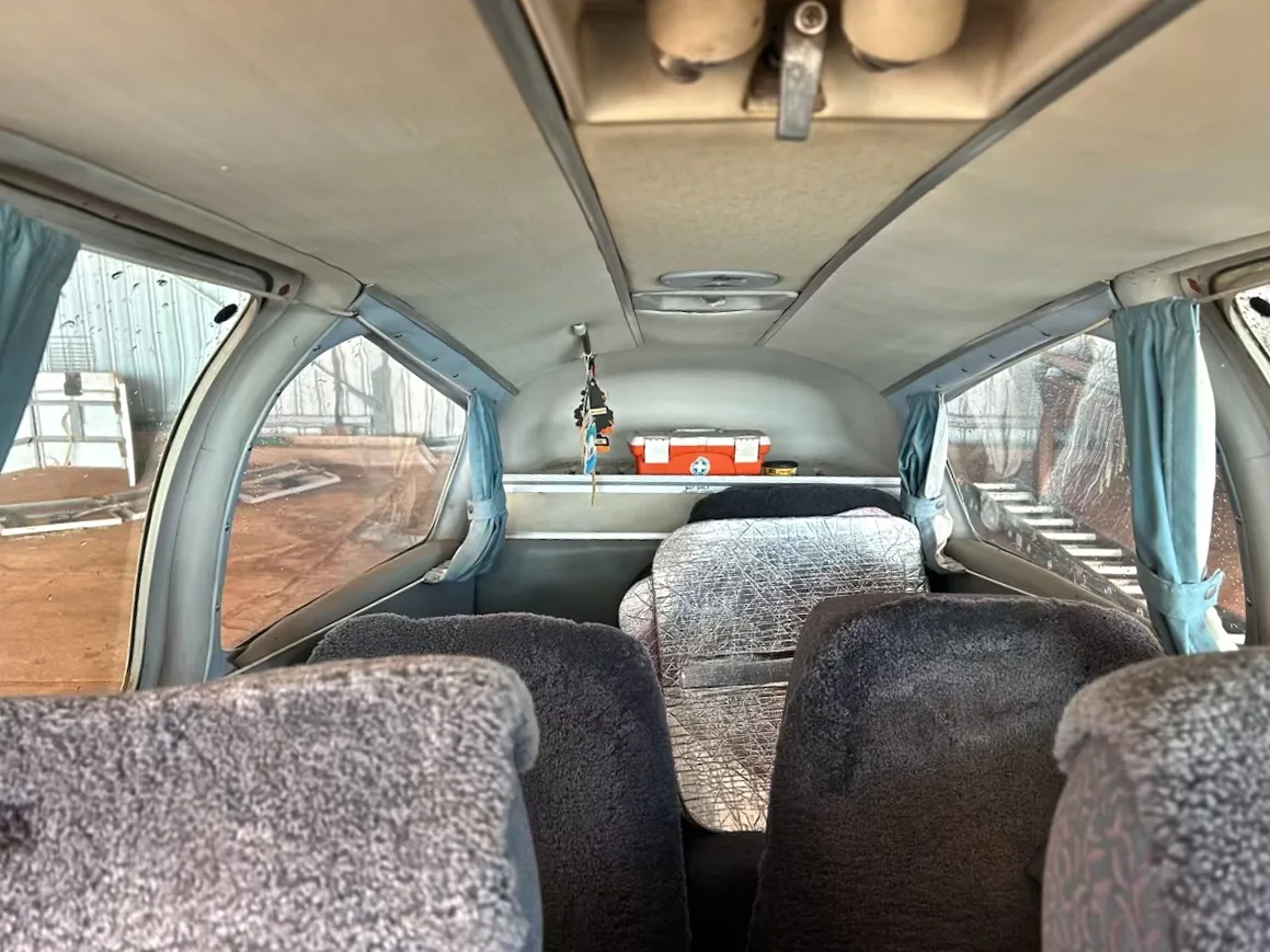 The interior cabin of a small aircraft with grey sheepskin seat covers and a red first aid kit in the rear.