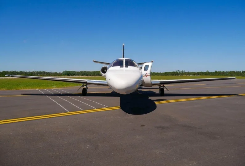 A head-on view of a white Cessna Citation business jet with its door open, parked on an asphalt runway under a clear blue sky.