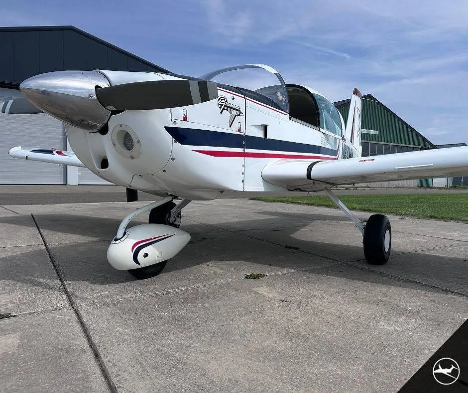 A close-up front view of the white Grumman AA-5B Tiger aircraft showing the propeller, nose gear, and cockpit.