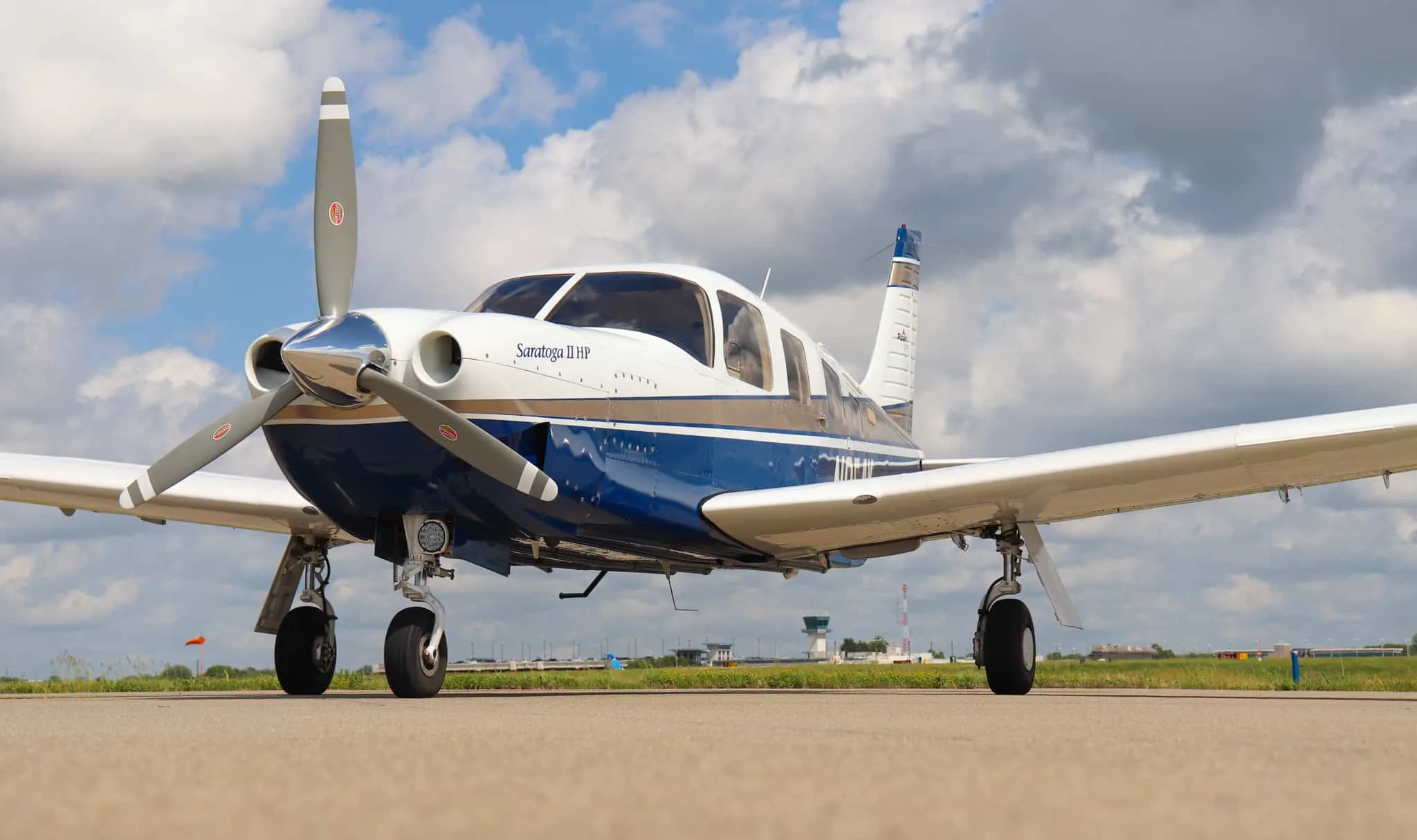 A low-angle front view of the Piper Saratoga II HP aircraft, N954K, with an airport tower in the background.