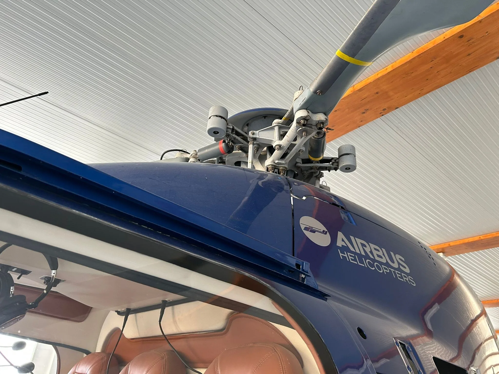 Close-up view of the main rotor and blue fuselage of an Airbus H120 Colibri helicopter, showing the Airbus Helicopters logo.