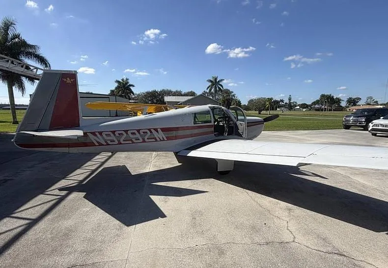 Side view of a white single-engine aircraft with red stripes, registration N9292M, parked with its door open.