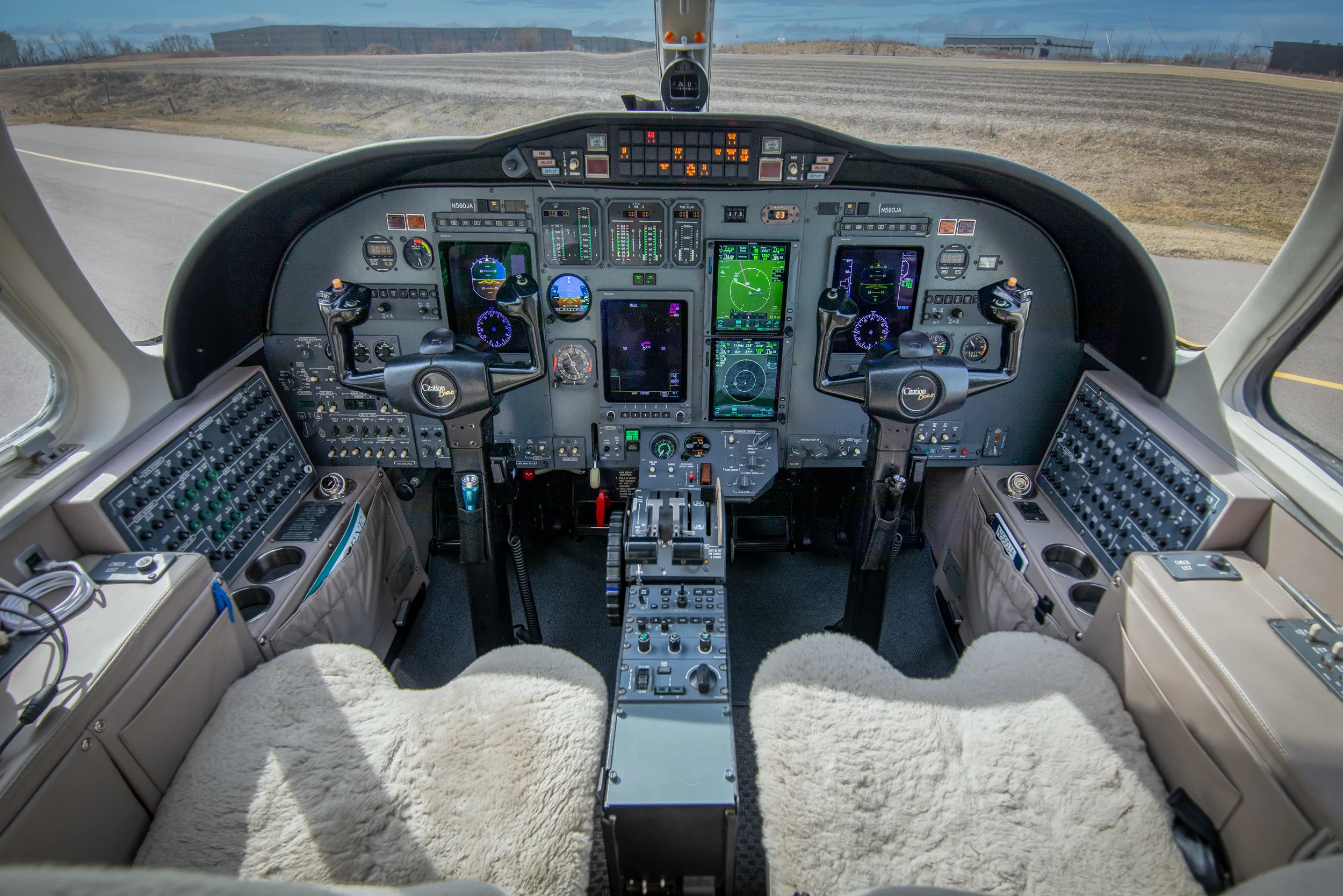The cockpit of a Cessna Citation Excel, featuring a modern glass panel display and sheepskin seat covers.