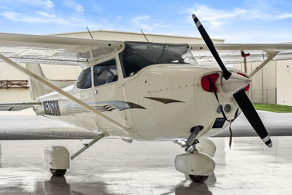 A close-up front view of the white Cessna 172, registration N5268H, with gold and gray stripes, in a hangar.