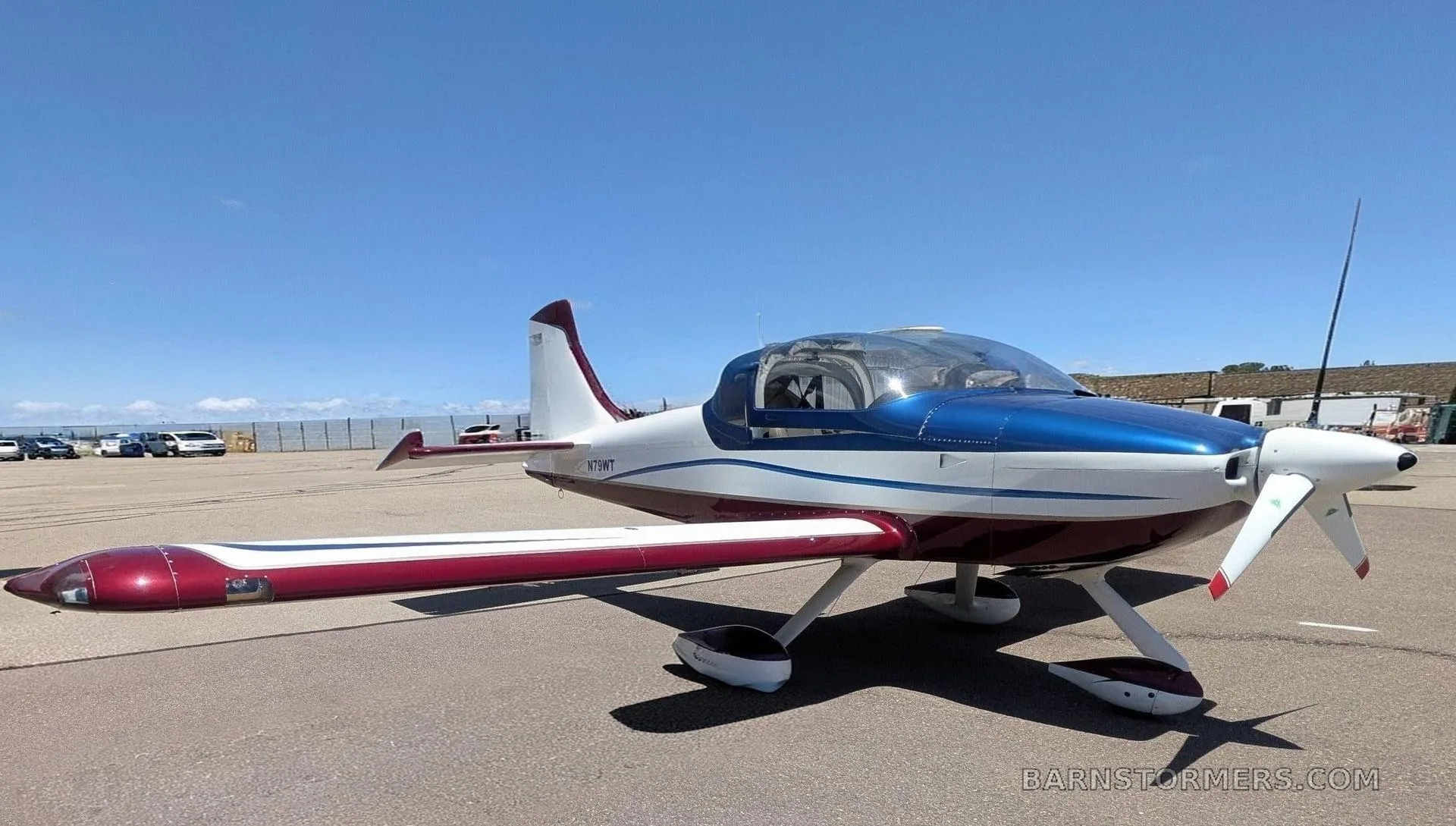 A white, blue, and red experimental aircraft (N79WT) with a bubble canopy is parked on an asphalt ramp under a clear blue sky.