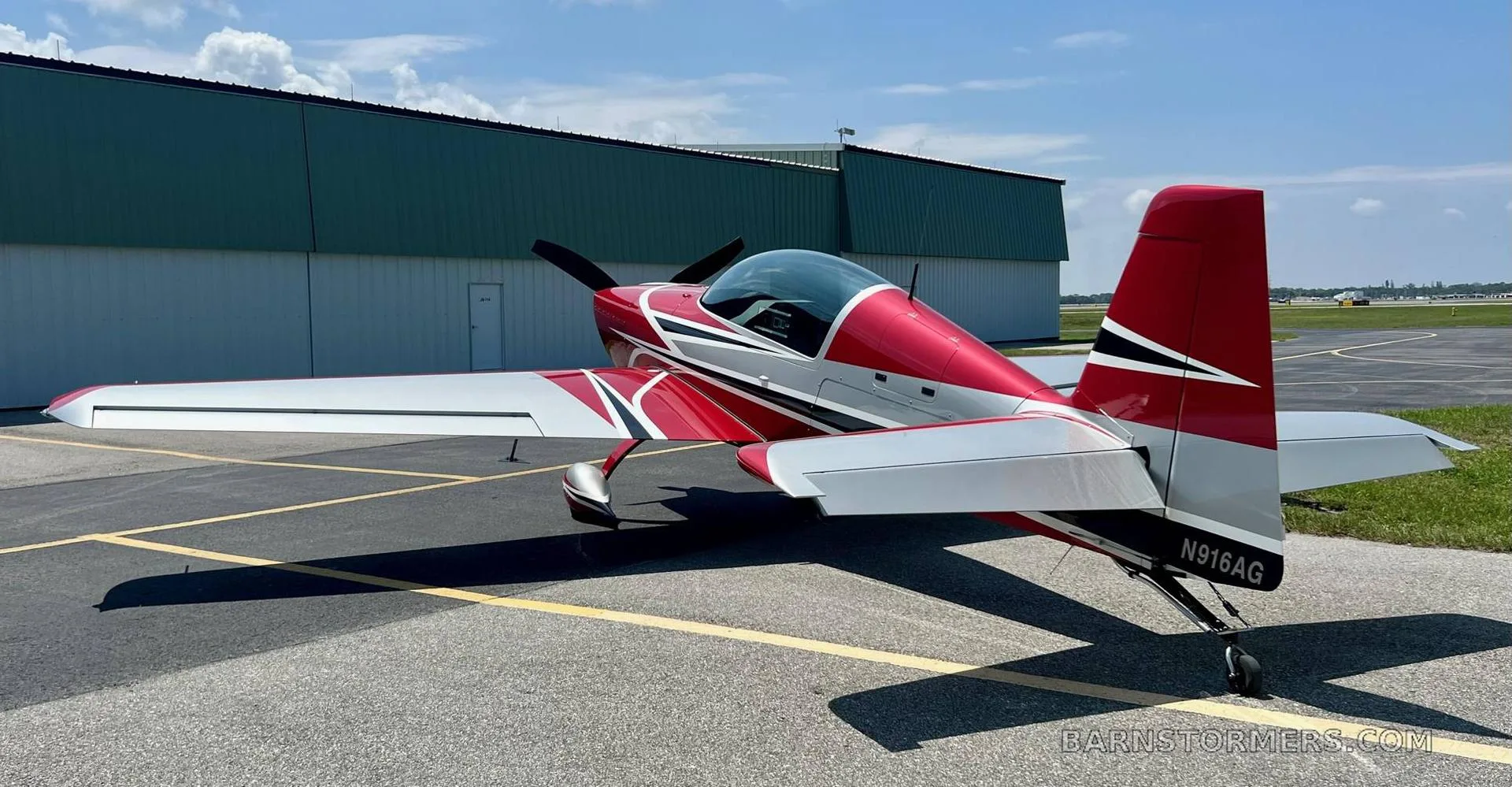A red and silver aerobatic aircraft with tail number N916AG is parked on an asphalt tarmac, viewed from the rear.