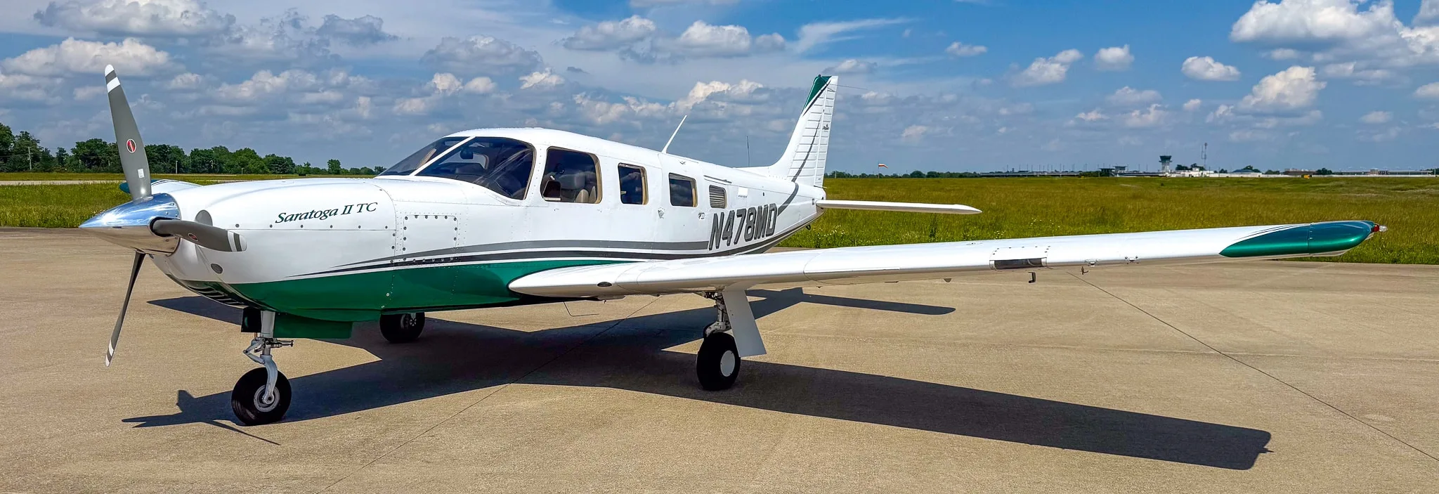 A white and green Piper Saratoga II TC aircraft (N478MD) parked on an airfield under a partly cloudy sky.