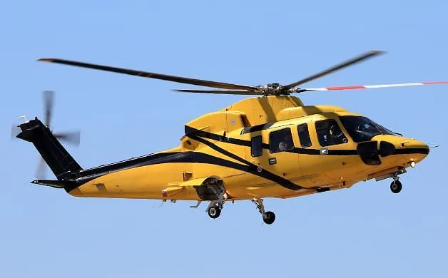 A yellow and black helicopter with its rotors spinning is captured in flight against a clear blue sky.