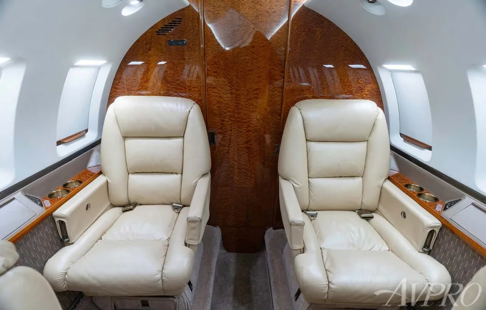Two beige leather seats face each other in the private jet's cabin, with polished wood paneling.