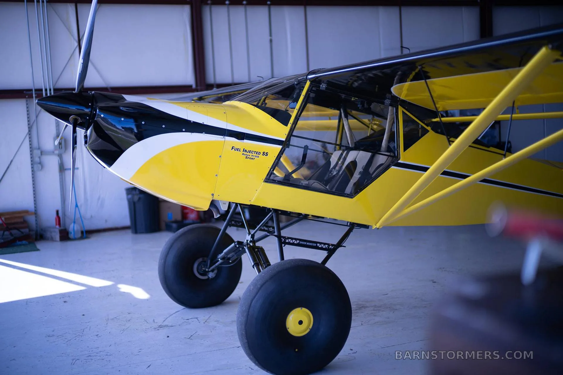 A yellow and black Kitfox aircraft with large tundra tires is parked inside a hangar.