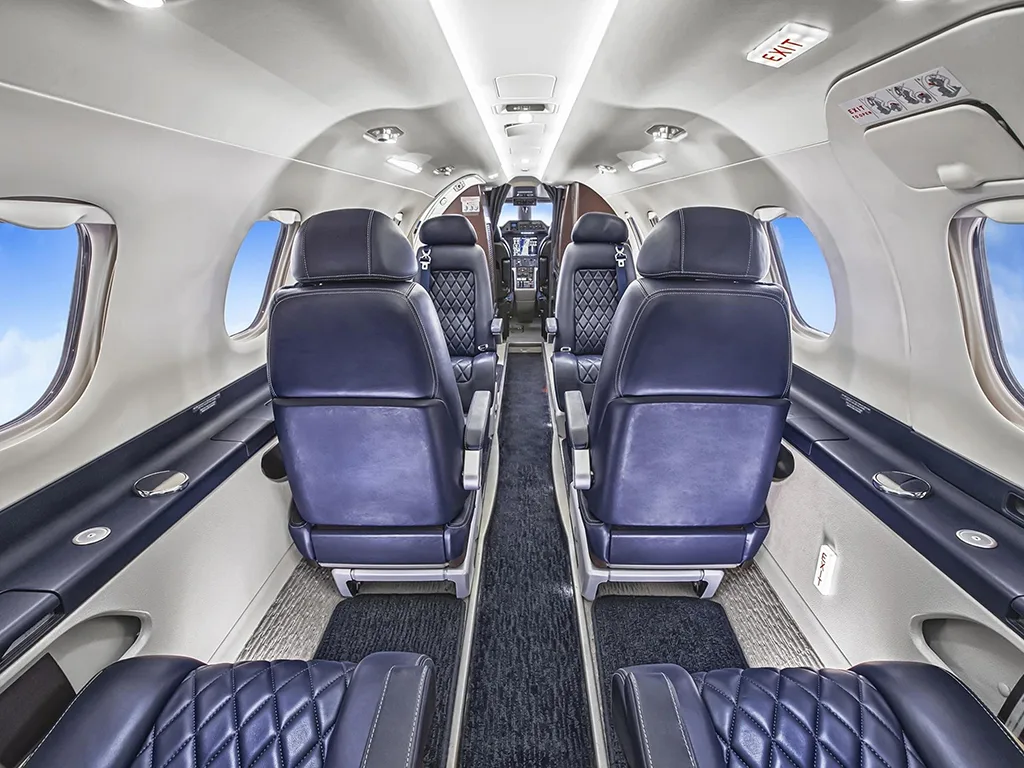 A view down the aircraft cabin aisle shows multiple rows of dark blue quilted leather seats and large windows.